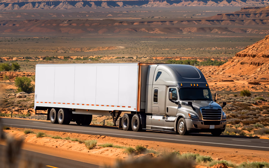 A tractor unit and dry van running a desert highway beneath red rock mesas